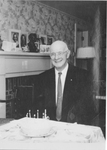Gleason Leonard Archer (President, 1937-1948, and Founder of Suffolk University) in front of birthday cake at his 79th birthday party, 3rd floor living room, Suffolk Law School, photograph, 29 October 1959