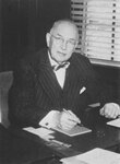 Suffolk University President Dennis C. Haley (1960-1965), seated behind desk, photograph, circa 1960s